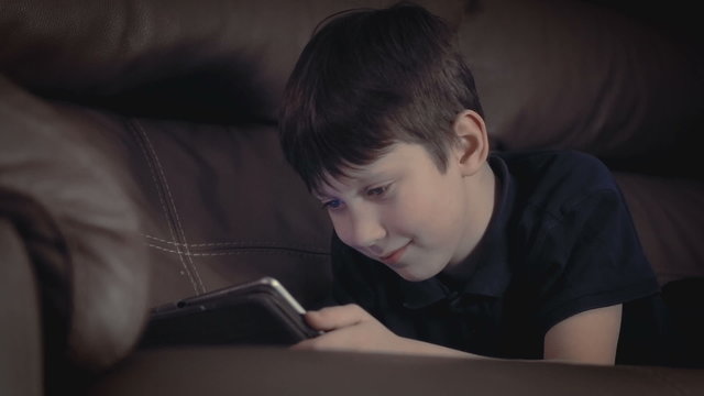 boy relaxing on sofa watching using playing games digital tablet surfing the net