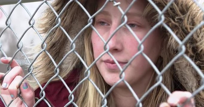 Female standing behind fence looking into distance, yearning for something that is missing.