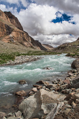 Mountain river between mountains above white clouds in Tibet region, China