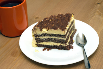 Breakfast. A piece of sponge cake on a white plate with a teaspoon and orange cup of tea on the wooden table surface. Photo closeup