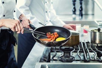 Zwei Köche in Hotelküche braten Gemüse in Pfanne
