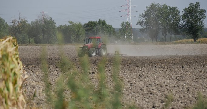 Tractor Distantly Tractor is Plowing The Field Flying Dust Cars are Passing by the Road along the Field High-Voltage Tower Blurred Image Branches