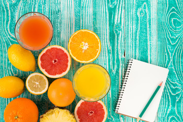 fresh juice in glass from citrus fruits - lemon, grapefruit, orange, pine apple and measuring tape and jotter with pencil on turquoise colored wooden background, top view
