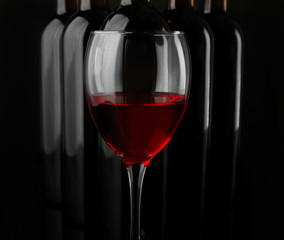 Red wine glass against bottles in a row on black background, close up