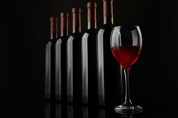 Red wine glass against bottles in a row on black background, close up