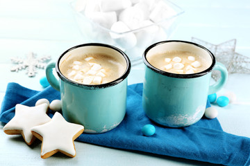 Two mugs of hot cacao with marshmallow, cookies and napkin on blue table