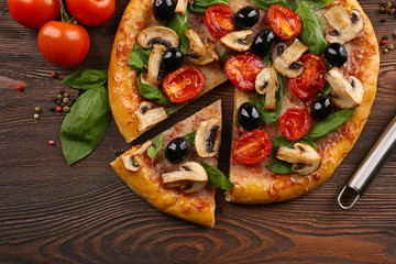 Sliced delicious tasty pizza with vegetables on wooden table