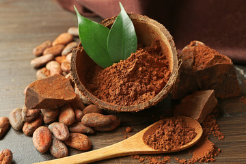 Bowl with aromatic cocoa powder and green leaf on wooden background, close up
