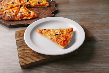 Slice of tasty pizza on white plate on wooden table, close up