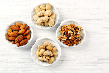 Pistachios, almonds, peanuts and walnut kernels in the bowls on white wooden table