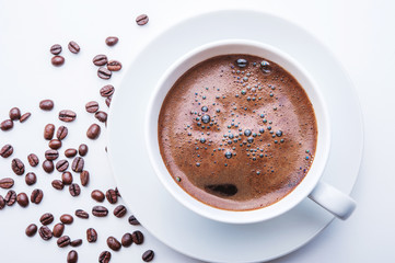 White cup of coffee with coffee beans on white table. Top view