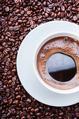 White cup of coffee on coffee beans. Top view