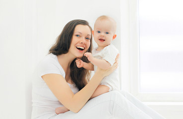 Happy smiling mother and baby at home in white room near window