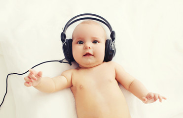 Beautiful baby listens to music in headphones lying on bed, top