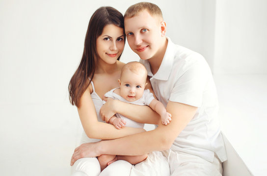 Happy family mother and father with baby at home in white room n