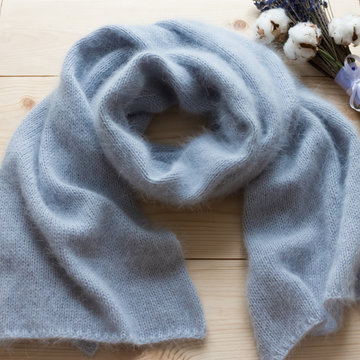 soft blue angora scarf tied by hand on natural wooden background with cotton branch