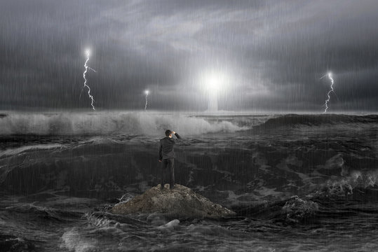 Man on rock gazing lighthouse in the ocean with storm