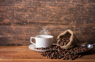 A cup of hot coffee, coffee beans on the stainless scoop and coffee bag on the wooden table, morning time, soften by window light, coffee concept