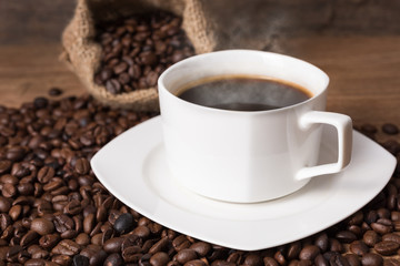 A cup of hot coffee, coffee beans on the stainless scoop and coffee bag on the wooden table, morning time, soften by window light, coffee concept