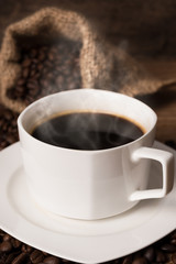 A cup of hot coffee, coffee beans on the stainless scoop and coffee bag on the wooden table, morning time, soften by window light, coffee concept
