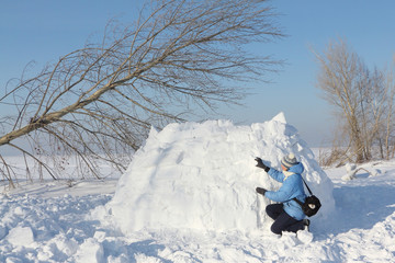 The woman in a blue jacket building an igloo on a snow glade in the winter 