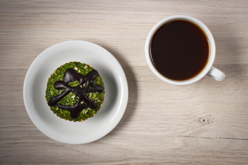 Fresh muffin with spinach, desiccated coconut, chocolate glaze and cup of coffee, delicious healthy dessert