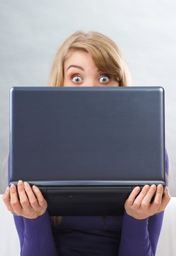 Scared woman holding laptop and looking out from behind computer