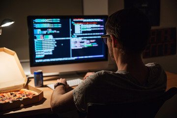 Back view of focused programmer writing code and eating pizza