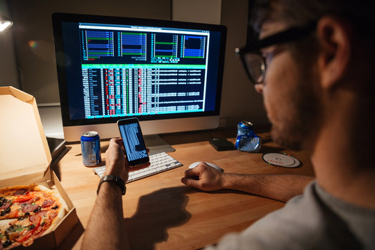 Serious developer in glasses using computer and smartphone