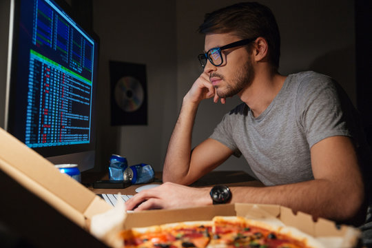 Pensive young developer in glasses coding at home