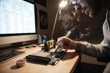 Serious man using scheme soldering iron for repairing motheboard