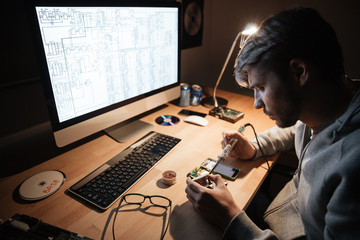 Serious man using soldering iron for fixing smartphone