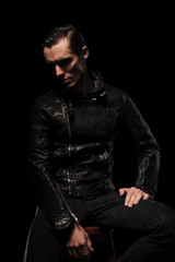 Fototapeta na wymiar punk model in leather jacket posing seated in dark studio