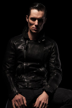 sexy biker in black leather jacket posing seated in dark
