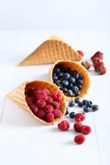 Waffle cones with berries on wooden table