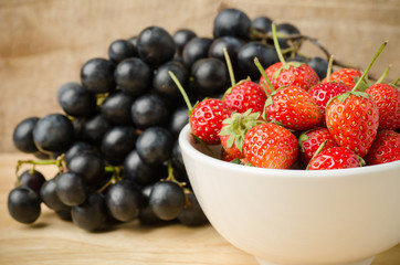Fresh strawberry in the bowl and grape on wooden background