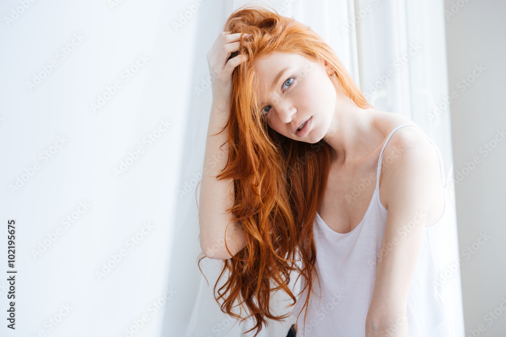 Wall mural Sensual woman with beautiful red hair standing near window