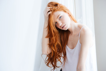 Sensual woman with beautiful red hair standing near window