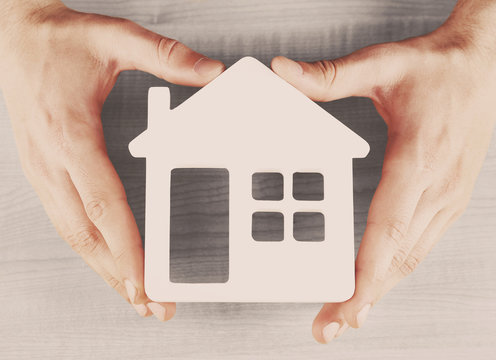 Male hands holding model of house on wooden background, close-up