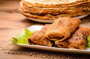 Stuffed pancakes on wooden background.