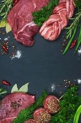 Different types of meat. Fresh butcher cut meat assortment on dark background. Decorated with vegetables and spice. Top view. Close-up