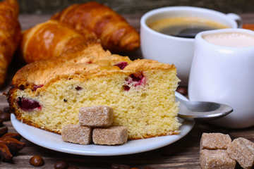 cup of coffee with cake with cranberries and croissants on a wooden background
