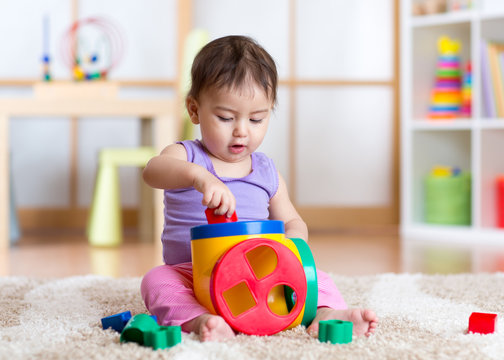 toddler girl playing indoors with sorter toy sitting on soft carpet
