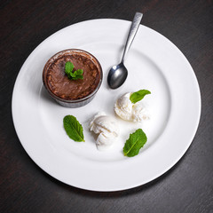 Warm dessert chocolate fondant lava cake served with vanilla ice cream balls and mint on white plate. Famous French dessert on dark wooden table top view