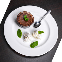 Warm dessert chocolate fondant lava cake served with vanilla ice cream balls and mint on white plate. Famous French dessert on dark wooden table top view.