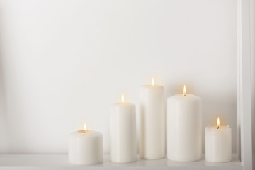 Fototapeta na wymiar white candles burning on a white shelf