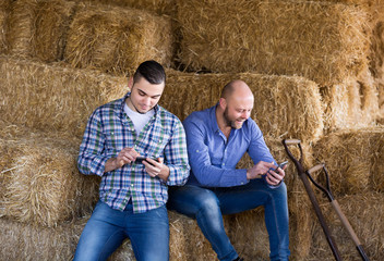 Naklejka na ściany i meble Two farmers with phones at hayloft