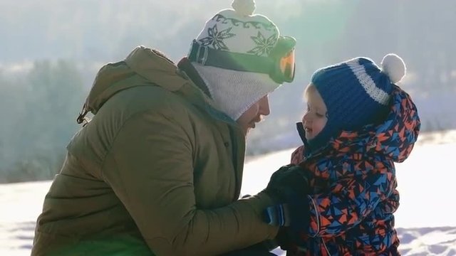 Affectionate father talking to his lovely baby son on cold winter day at ski resort 