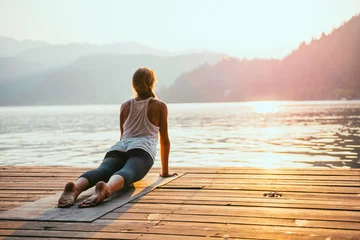 Foto op Plexiglas Yogaschool Yoga zonnegroet. Jonge vrouw die yoga doet bij het meer bij zonsondergang