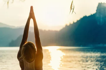 Fototapete Rund Saluting to the sun. Young woman doing yoga by the lake at sunset © Microgen